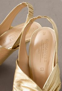 Gouden slingback sandalen van glanzend materiaal, met bijeen geraapte banden en een gladde binnenzool. Merken zijn op de binnenzool geperst.