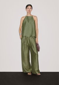 Olive green, sleeveless top with a flowing design, paired with loose, matching trousers. Accessories include a braided, burgundy clutch.