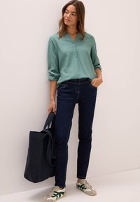 Ljusgrön skjorta med uppvikta ärmar, kombinerad med mörkblå jeans. Outfiten kompletteras av en marinblå tote-väska och sneakers.