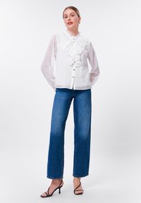 White polka dot blouse with ruffled collar and button closure, paired with blue wide-leg jeans and black stiletto sandals.