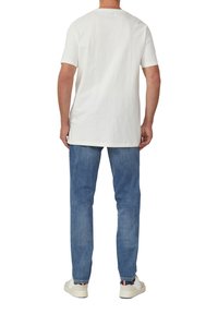 Weißes Baumwoll-T-Shirt, kurze Ärmel, gerader Schnitt, kombiniert mit hellblauen Jeans und weißen Sneakers mit dezenten Farbakzenten.