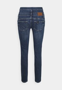 Jeans de mezclilla azul con un diseño ajustado, cinco bolsillos y una etiqueta de cuero en la parte trasera de la cinturilla. Textura suave y corte de pierna recta.