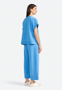 Niebieski, oversize bluza i szerokie spodnie. Gładka tekstura materiału, projekt z opadającymi ramionami i ściągacze na rękawach. Białe buty z beżowymi akcentami.