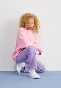 Sweatshirt oversized rosa com punhos canelados, combinado com calças largas lilás. Ténis brancos com toques de lavanda.
