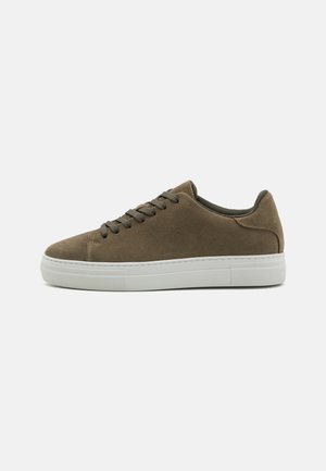 Brown suede sneaker with a rounded toe, flat white rubber sole, and matching lace details. Minimalist design with stitching accents.