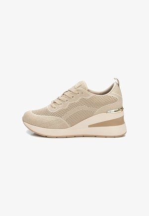 Sneaker atletico beige con tomaia in mesh, punta arrotondata e suola a zeppa. Presenta motivi testurizzati e un accento metallico sul tallone.