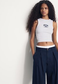 Sivý bavlnený crop tank top s nápisom "BOSTON 1931 ATHLETIC CREW" vytlačeným v námorníckej modrej farbe, kombinovaný s námorníckymi širokými nohavicami s bielym pásom.