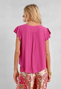 Top rosa con maniche a flutter e orlo curvo, dotato di dettaglio arricciato sul retro, realizzato in un tessuto morbido, abbinato a pantaloni a gamba larga con fantasia.