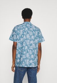 Camisa de manga corta en azul claro con un patrón de palmeras. Cuenta con un cuello clásico y un corte relajado, confeccionada con una tela ligera.