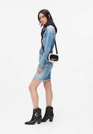 Denim jacket and skirt in light blue, black ankle boots, and a small black and white fluffy crossbody bag with logo.