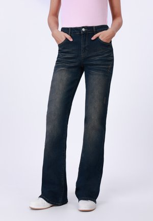 Dark blue flared jeans with a faded finish, five pockets, and stitching accents, paired with white sneakers.