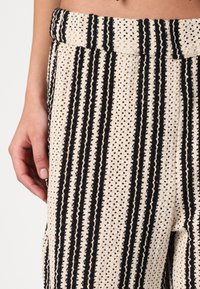 Knit pants with a wide elastic waistband, featuring a cream base and vertical black stripes. Textured, loose fit with side pockets.