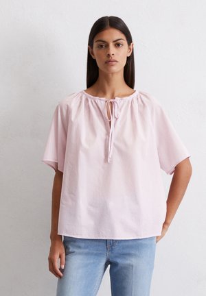 Lichtroze katoenen blouse met een ronde halslijn, gecrepeerde details en korte mouwen. Heeft een striksluiting bij de nek en een losse pasvorm.