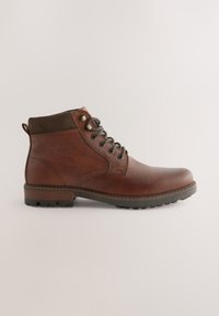 Brauner Lederknöchelstiefel mit dunklen Schnürsenkeln, gepolstertem Kragen und Gummisohle, von der Seite auf einfarbig hellem Hintergrund gezeigt.