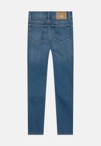 Jeans ajustados de corte slim, de color azul oscuro con una textura ligeramente deslavada. Cuenta con cuatro bolsillos y una etiqueta de cuero marrón en la cintura.