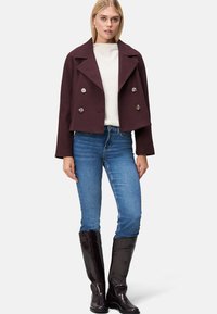 Bordeaux cropped double-breasted jakke med sølvknapper, parret med en cremefarvet sweater, blå jeans og knæhøje glansfulde sorte støvler.