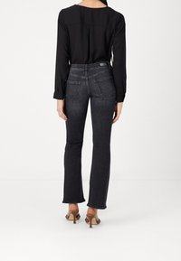 Haut noir à manches longues associé à un jean évasé à lavage foncé. Le jean comporte des poches arrière et des détails de couture subtils, porté avec des sandales à talons beiges.