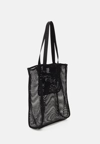 Svart nätväska med breda öppningar, som har hållbara remmar och en strukturerad form. Texturerat material med ett mönstrat design.