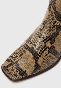 Bottines imprimé serpent avec un bout pointu, présentant une combinaison de textures noire et tan. Fini en cuir lisse et design structuré.