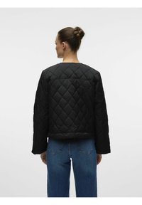 Juodas siuvinėtas švarkas su apvaliu kaklu ir ilgomis rankovėmis. Nugaros dalyje yra deimanto formos siuvinėjimas, kartu su mėlynos džinsinės kelnėmis.