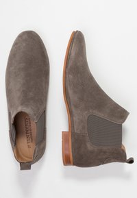 Bottines en suède gris avec des panneaux latéraux élastiques et un talon en bois brun. Le design présente un bout arrondi et des détails de couture minimalistes.