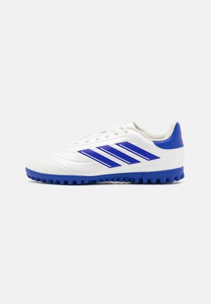 Zapatos de fútbol blancos con acentos azules, que cuentan con tres rayas azules, una parte superior texturizada y una suela de goma diseñada para tracción.
