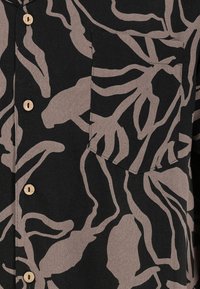 Button-up shirt in black fabric featuring a tan abstract pattern. Includes a chest pocket with a pointed flap and natural wooden buttons.