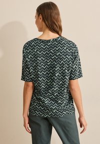 Svart och grön t-shirt med zigzag-mönster och avslappnad passform, korta ärmar, tillverkad av lättviktsmaterial, med rundad halsringning.