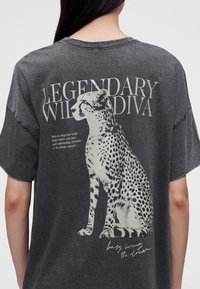 Dos d'un t-shirt gris foncé avec un graphisme blanc d'un guépard assis, grand texte "Legendary Wild Diva," et phrases motivantes plus petites.