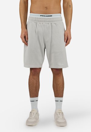 Mand iført lysegrå ribbet shorts, hvide sokker med sort tekst og beige sneakers, stående mod hvid baggrund.