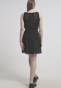 Mustapuku, jossa on pitsitausta, tiukka vyötärö ja hulmuava helma. Kangas on kevyt ja sileä. Yhdistetty mustiin kenkiin.