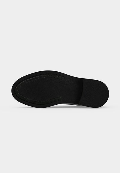 Semelle de chaussure noire vue d'en bas montrant une surface lisse avec des détails cousus autour des zones des orteils et du talon.