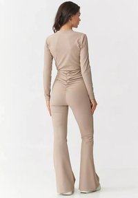 Beżowa bluzka z długim rękawem w połączeniu z dopasowanymi, rozszerzającymi się spodniami. Gładki, rozciągliwy materiał z marszczeniem z tyłu, tworzący elegancką sylwetkę.