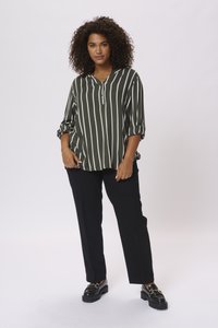 Blouse ray�ée vert olive avec un col henley à boutons, manches retroussées, associée à un pantalon noir et des mocassins noirs épais.