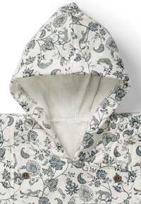 Huvtröja med blommönster som har en texturerad vit innerfoder och dekorativ knappdetalj fram.