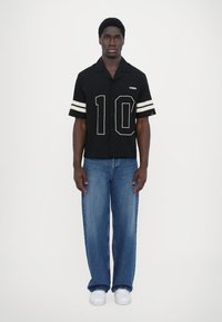 Black short-sleeve shirt with white stripes and number "10" on the front, paired with light blue baggy jeans and white sneakers.