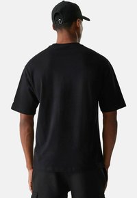 T-shirt en coton noir à coupe décontractée, à manches courtes et à ourlet droit. Vu de l'arrière, mettant en avant un design simple et épuré.