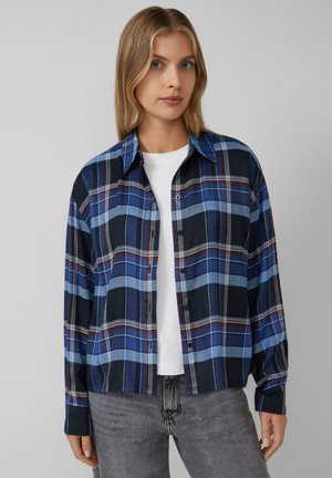 Long-sleeve plaid shirt in blue, black, and burgundy. Features a button-down front, pointed collar, and lightweight fabric. Worn over a white shirt.