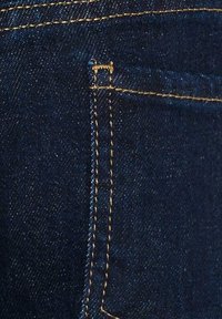 Donkerdenim jeans met gouden stiksels, met een klein achterzakje en een gladde textuur, waarop een close-up van de stof en naaddetails te zien is.