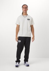 Relaxed-fit cream cotton T-shirt with black print "1894" and loose black sweatpants. Features a simple design and crew neckline.
