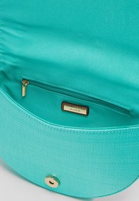 L'interno di una borsa a mano circolare turchese presenta una fodera in tessuto liscio, una tasca con zip e una placca con logo in hardware dorato.