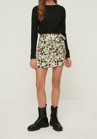 Jupe mini à motifs floraux avec une base noire, ornée d'accents verts et oranges. Associée à un haut ajusté à manches longues noir et des bottes de combat noires.