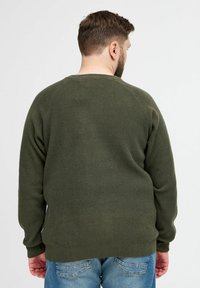 Sweatshirt en tricot vert olive avec une finition texturée, manches raglan et encolure côtelée, associé à un jean en denim bleu.