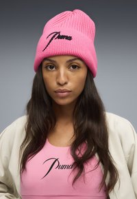 Roze gebreide beanie met een geribbelde textuur en geborduurd zwart Puma logo. Combineren met een lichtroze top met hetzelfde logo.