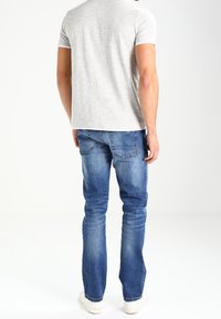 T-shirt grigio a maniche corte abbinato a jeans in denim blu. I jeans presentano una vestibilità classica con leggere sfumature e tasche posteriori. Sneakers bianche visibili.