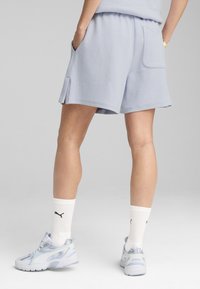 Lichtblauwe shorts met wafeltextuur en een relaxte pasvorm, zijzakken en zijopeningen. Gecombineerd met witte sokken en lichtblauwe sportschoenen.