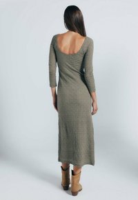 Olivengrünes, langärmliges, tailliertes Kleid mit runder Rückenpartie, strukturiertem Stoff und Midi-Länge; kombiniert mit beigefarbenen Knöchelboots.