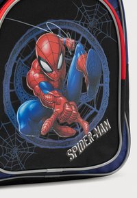 Μαύρο σακίδιο πλάτης με γραφικό Spider-Man σε κόκκινο και μπλε, με λεπτομέρειες σχεδίου ιστού αράχνης. Περιλαμβάνει λευκό κείμενο με τη λέξη "SPIDER-MAN". Υφή στην επιφάνεια.
