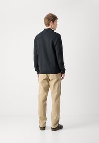 Suéter de punto negro con una textura sutil y cuello, combinado con pantalones cargo beige con bolsillos laterales y zapatos oscuros.
