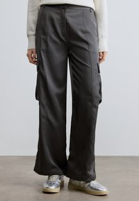 Sivé saténové cargo nohavice voľného strihu s bočnými vreckami a hladkou textúrou. Kombinované so striebornými teniskami a krémovým svetrom.